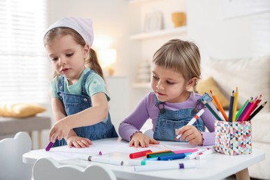 Cute little sisters drawing at white table in room