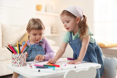 Cute little sisters drawing at white table in room