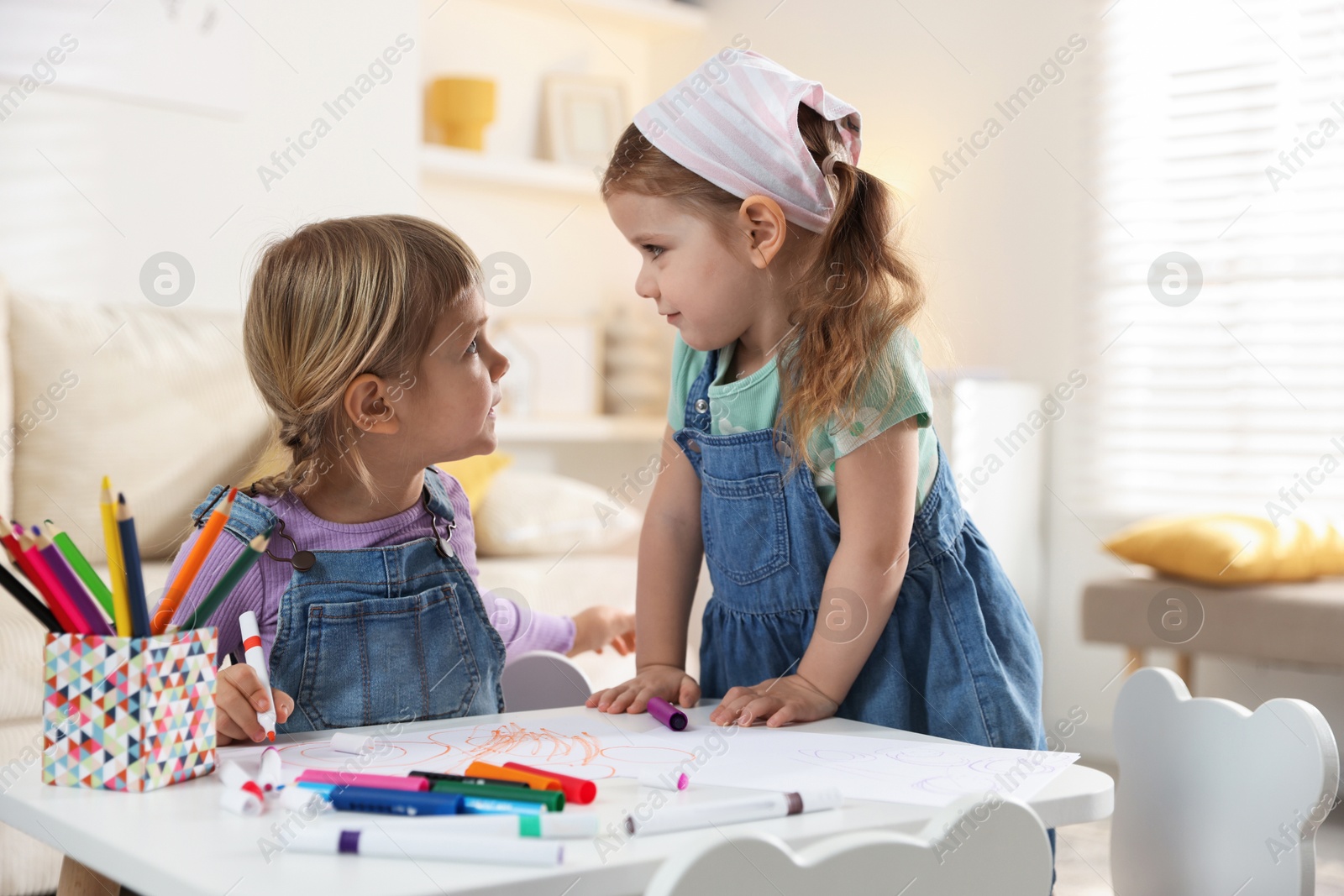 Photo of Cute little sisters drawing at white table in room