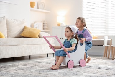 Cute little sisters playing with toy stroller at home