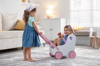 Cute little sisters playing with toy stroller at home