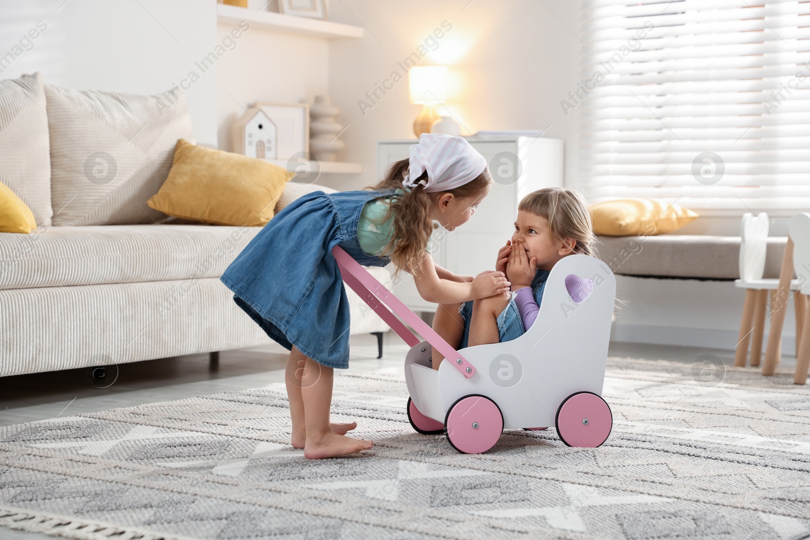 Photo of Cute little sisters playing with toy stroller at home