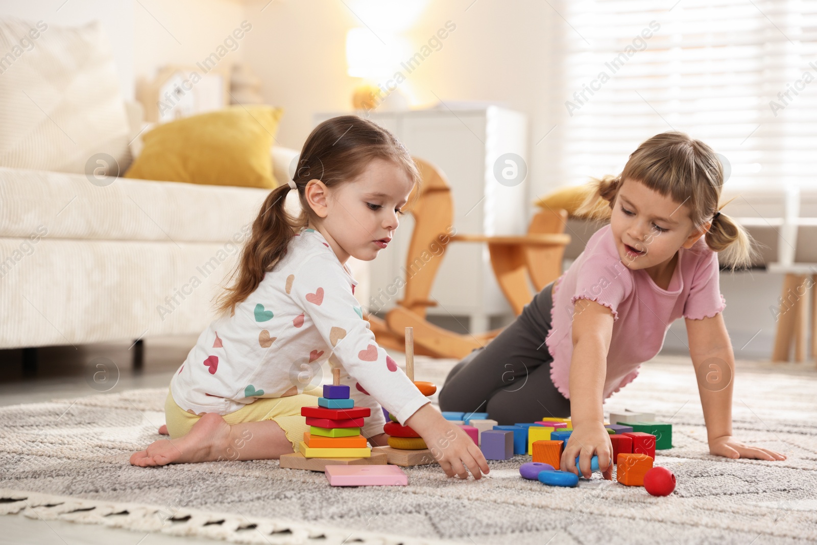 Photo of Cute little sisters playing with toy pyramids on floor at home