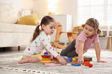 Cute little sisters playing with toy pyramids on floor at home