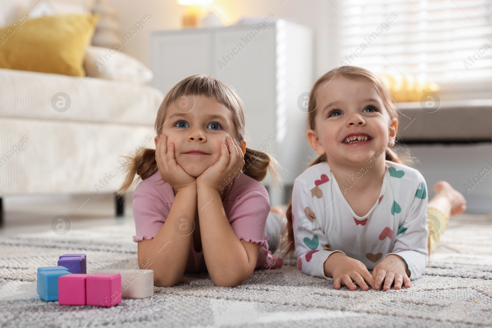 Photo of Cute little sisters lying on floor at home