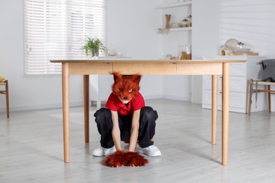 Photo of Quadrobics. Boy wearing fox mask and gloves under table indoors