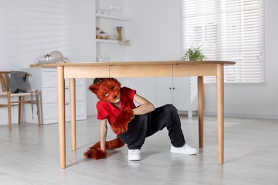 Quadrobics. Boy wearing fox mask, tail and gloves under table indoors