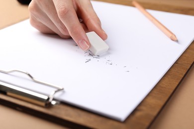 Photo of Woman rubbing eraser against paper at brown table, closeup