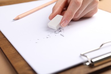 Photo of Woman rubbing eraser against paper at brown table, closeup