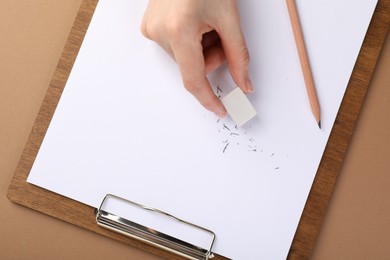 Photo of Woman rubbing eraser against paper at brown table, top view