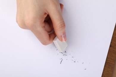 Photo of Woman rubbing eraser against paper at brown table, top view