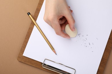 Photo of Woman rubbing eraser against paper at brown table, top view