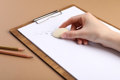 Photo of Woman rubbing eraser against paper at brown table, closeup