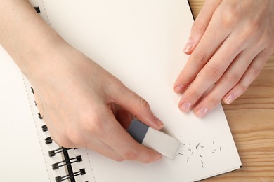 Photo of Woman rubbing eraser against paper at wooden table, top view