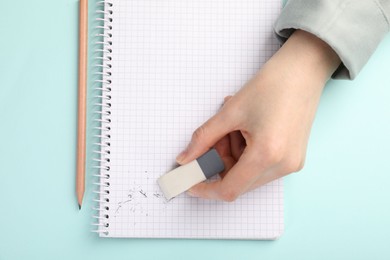 Photo of Woman rubbing eraser against paper at light blue table, top view