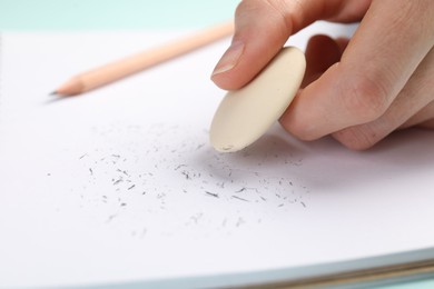 Photo of Woman rubbing eraser against paper at light blue table, closeup