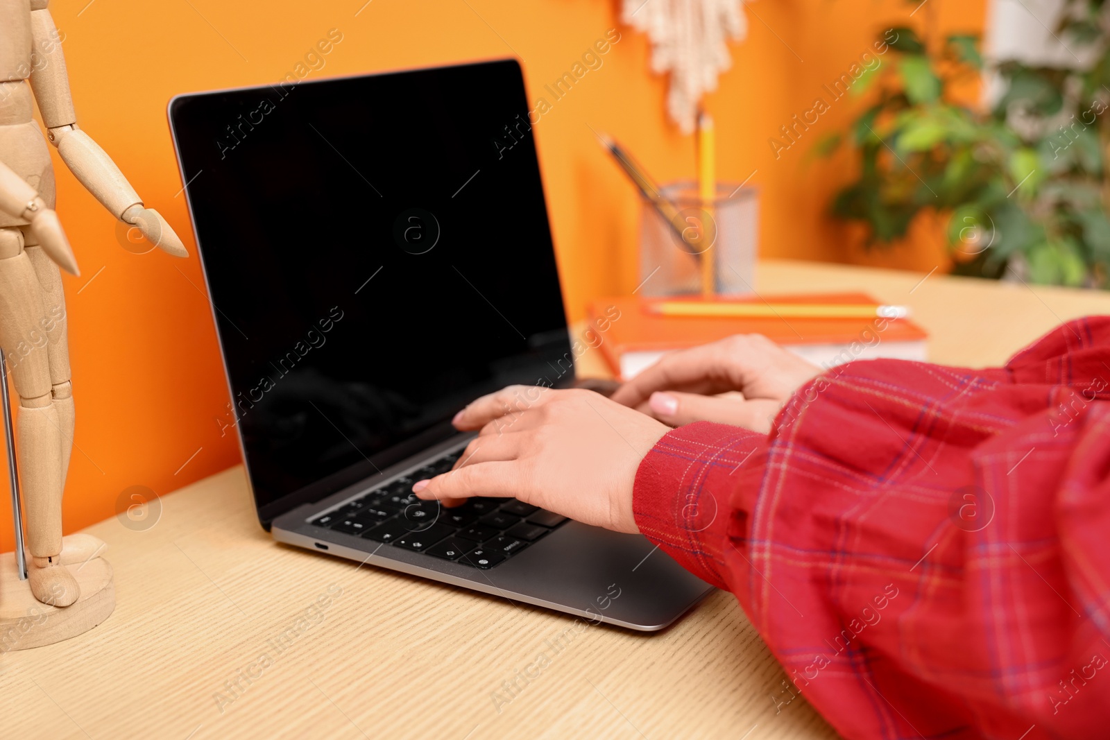 Photo of Woman working on laptop at wooden desk indoors, closeup