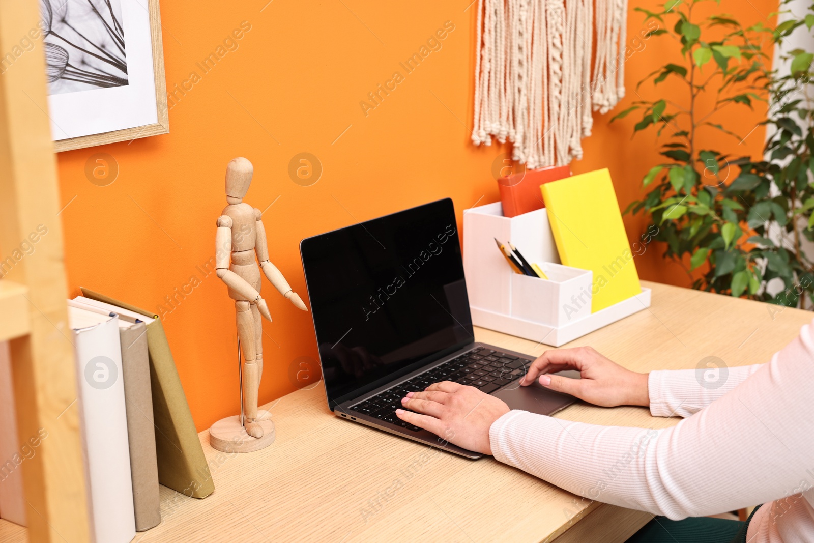 Photo of Woman working on laptop at wooden desk indoors, closeup