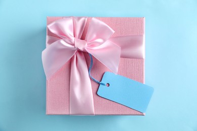 Photo of Gift box with blank tag on light blue background, top view