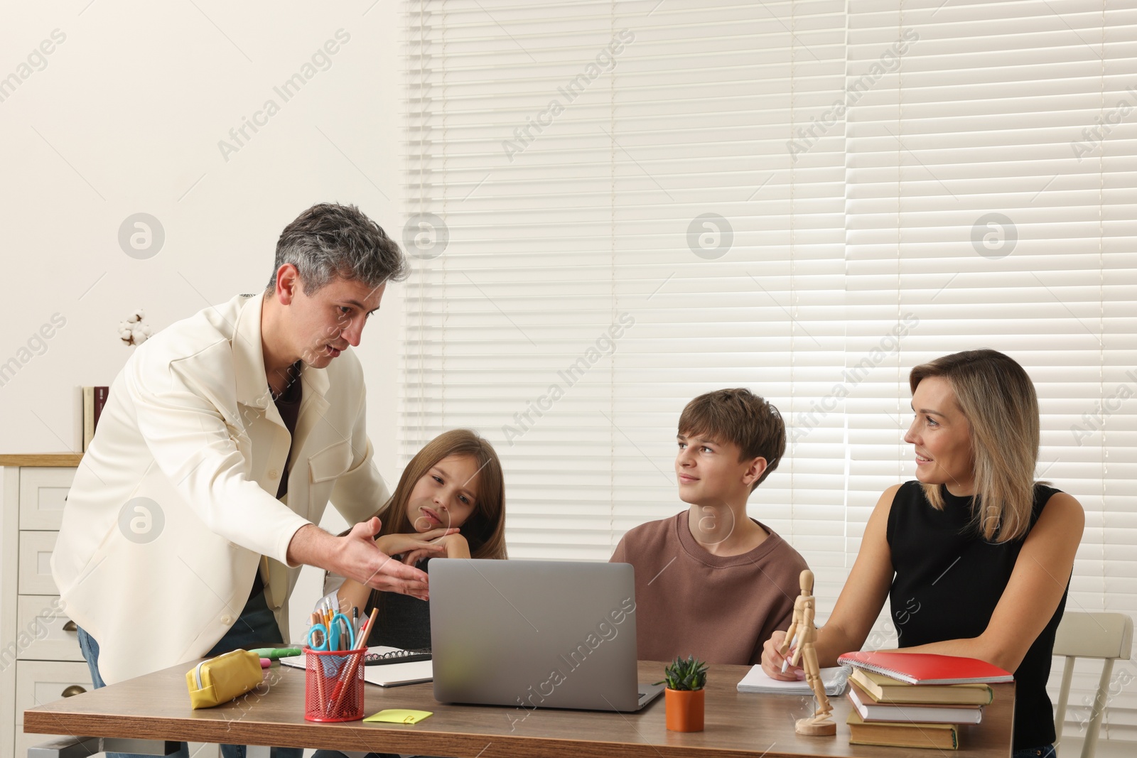 Photo of Parents and their children doing homework with laptop at table indoors