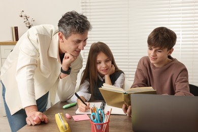 Photo of Father helping his children with homework at table indoors