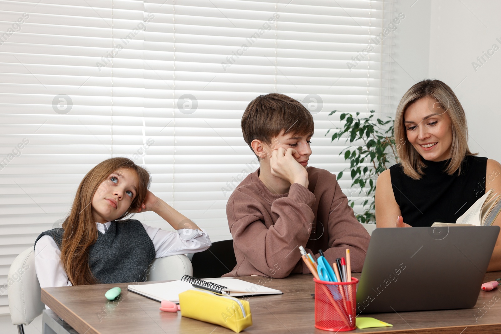 Photo of Smiling mother helping her children with homework at table indoors