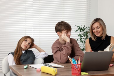 Smiling mother helping her children with homework at table indoors