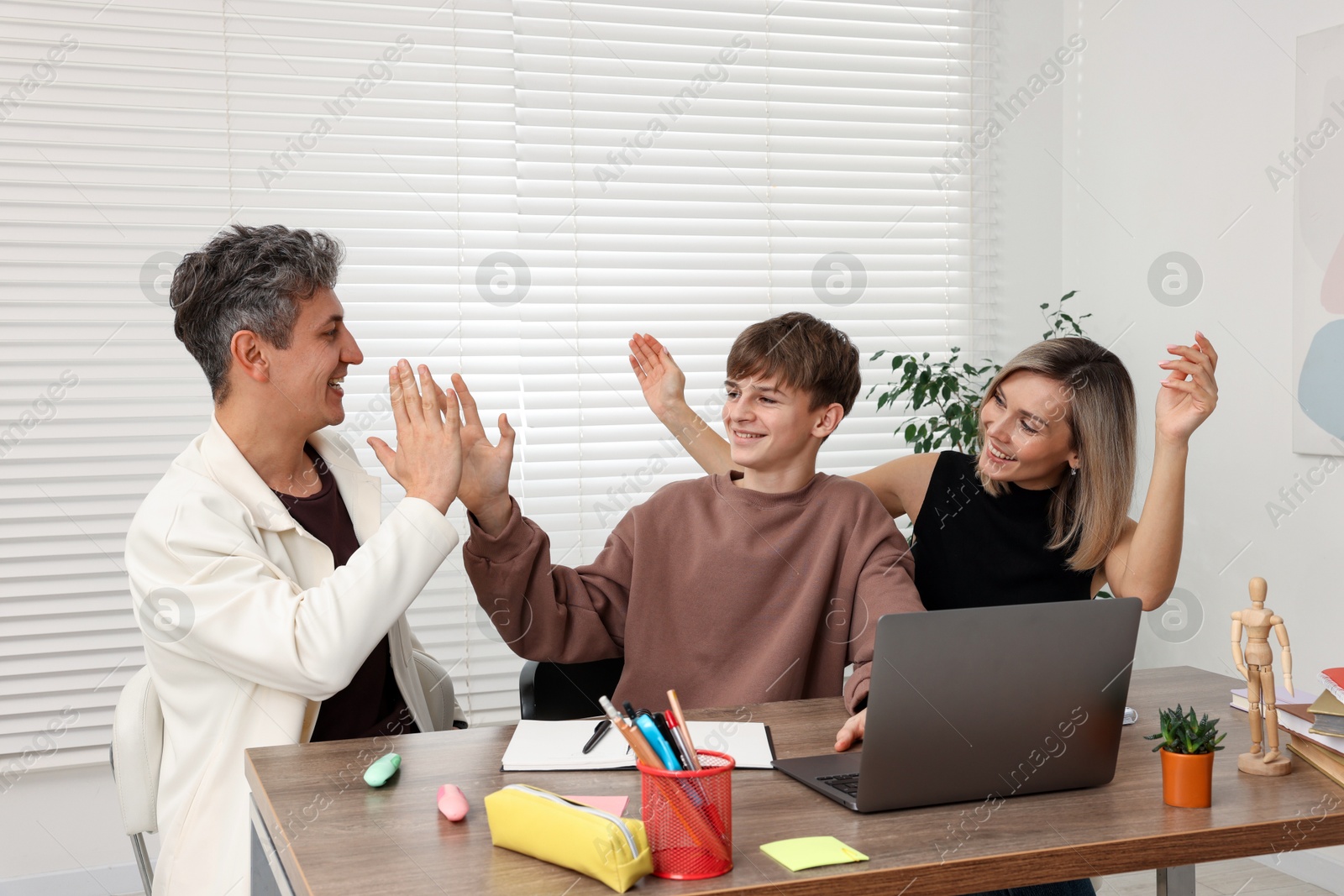 Photo of Smiling parents and their son doing homework with laptop at table indoors