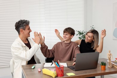 Photo of Smiling parents and their son doing homework with laptop at table indoors