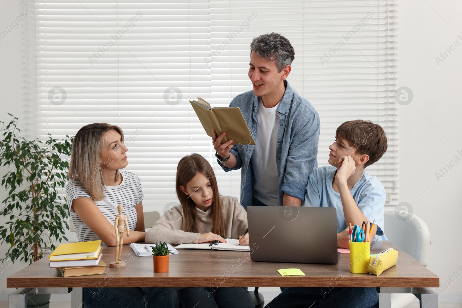 Photo of Parents and their children doing homework with laptop at table indoors