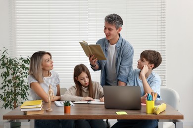 Parents and their children doing homework with laptop at table indoors