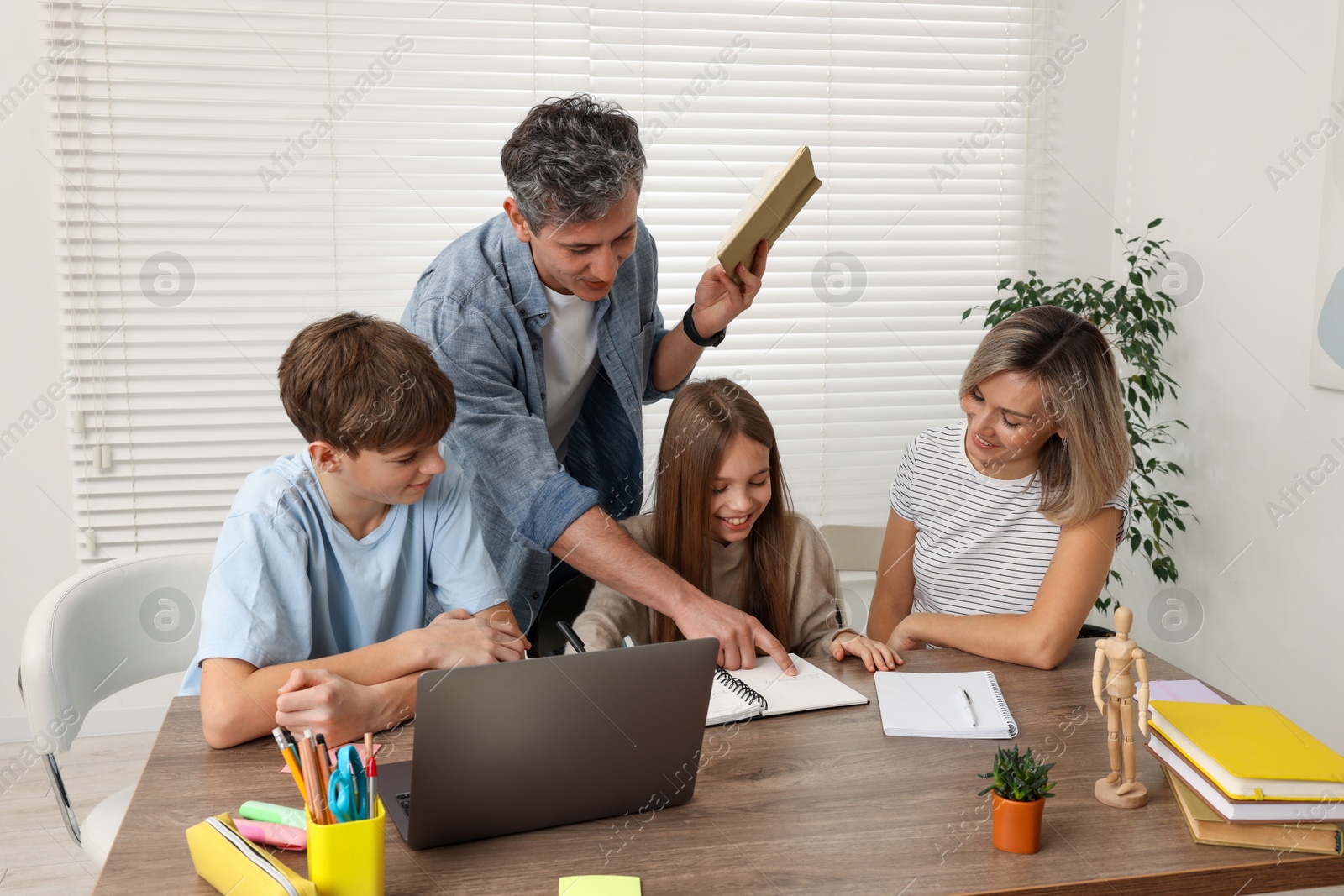 Photo of Parents and their children doing homework with laptop at table indoors