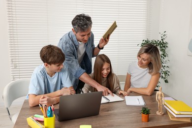 Photo of Parents and their children doing homework with laptop at table indoors