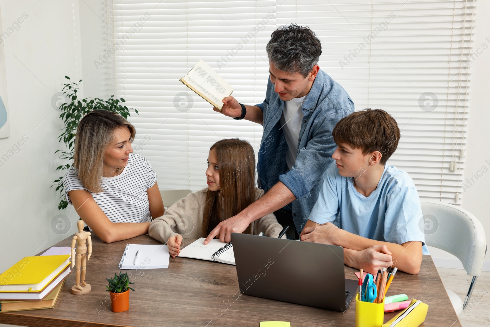 Photo of Parents and their children doing homework with laptop at table indoors