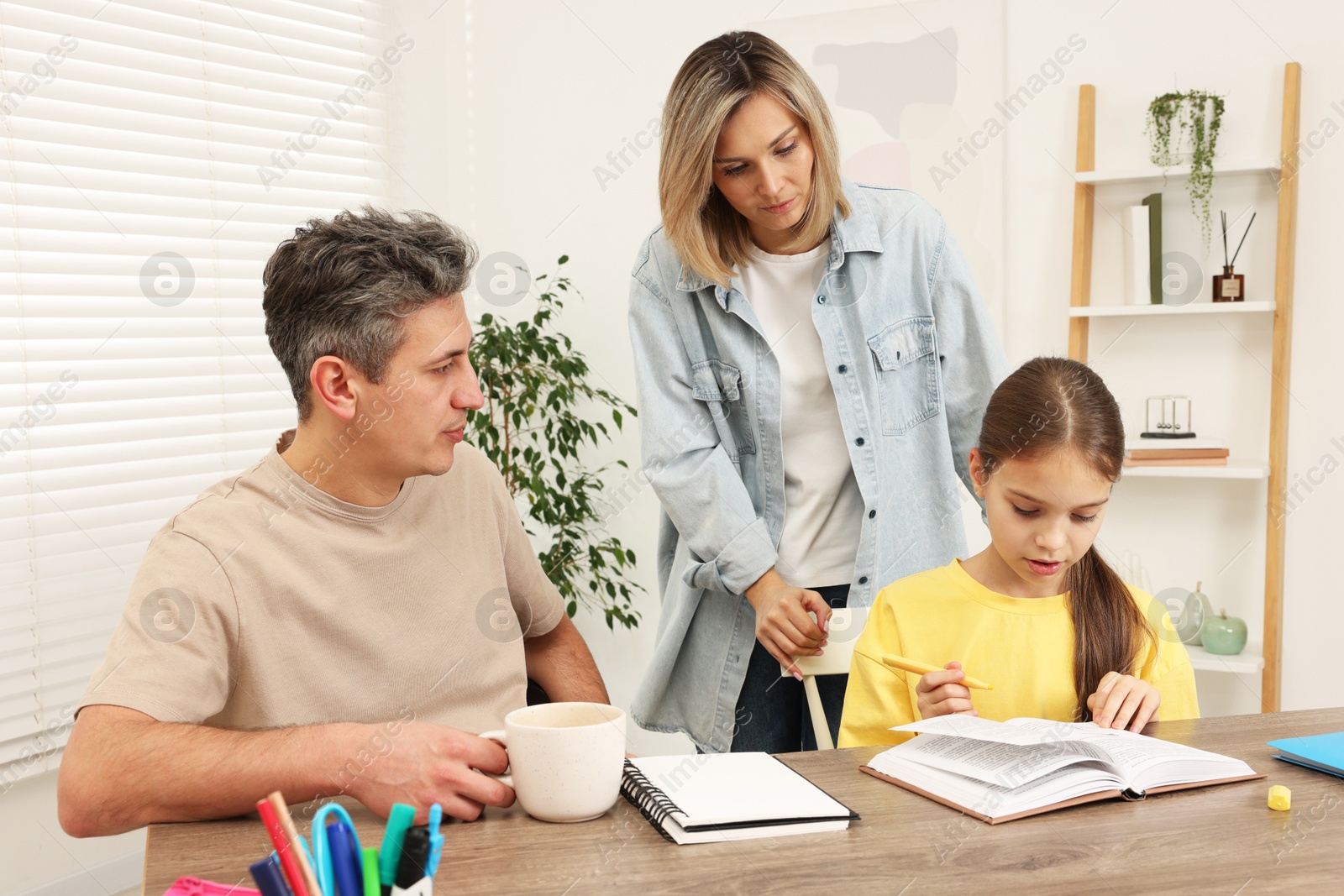 Photo of Parents helping their daughter with homework at table indoors