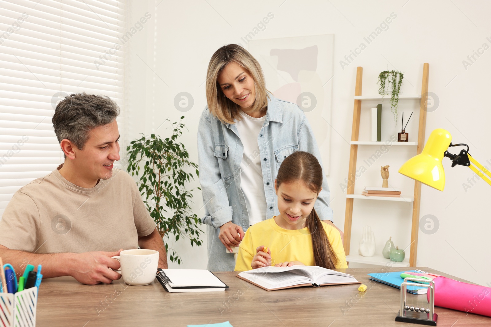 Photo of Smiling parents helping their daughter with homework at table indoors