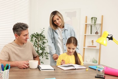 Smiling parents helping their daughter with homework at table indoors