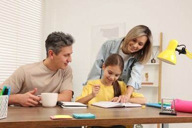 Photo of Smiling parents helping their daughter with homework at table indoors