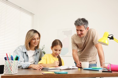 Smiling parents helping their daughter with homework at table indoors