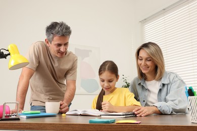 Photo of Smiling parents helping their daughter with homework at table indoors