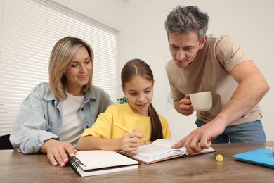 Photo of Parents helping their daughter with homework at table indoors