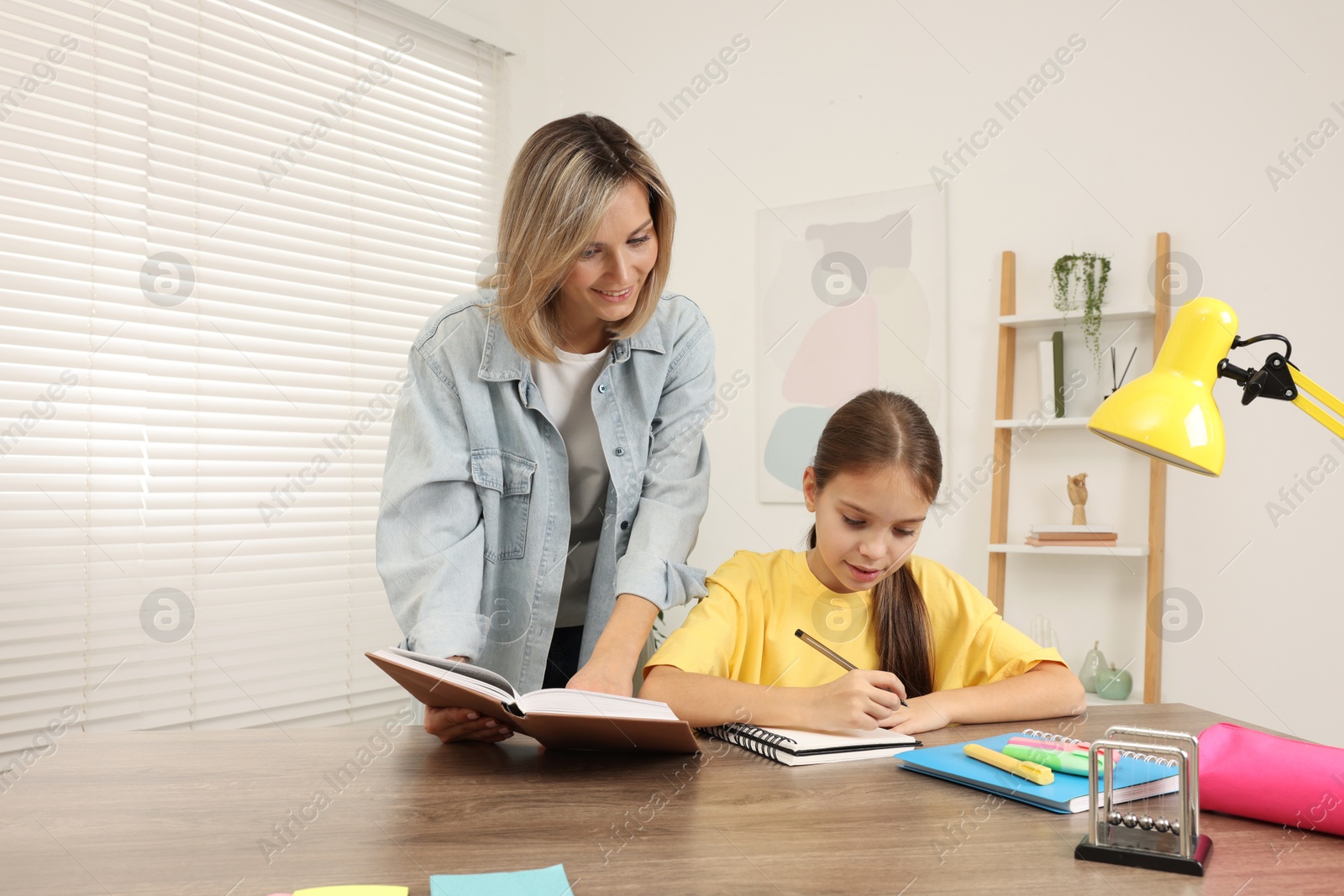 Photo of Smiling mother helping her daughter with homework at table indoors