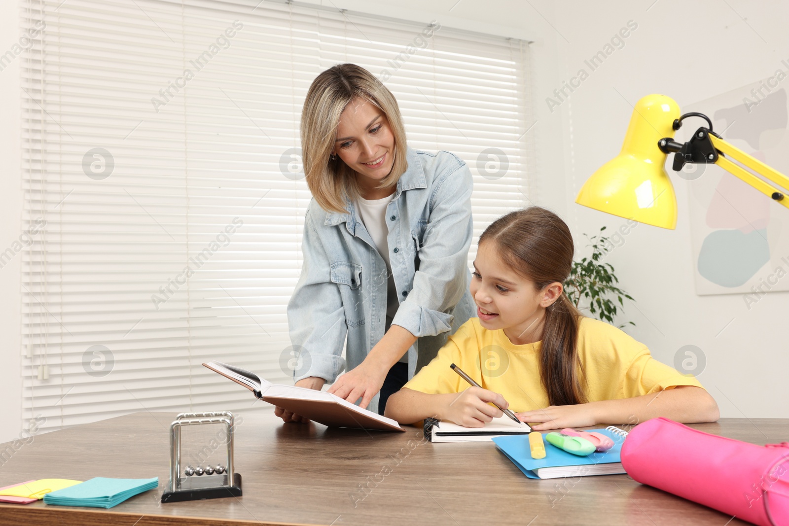 Photo of Smiling mother helping her daughter with homework at table indoors