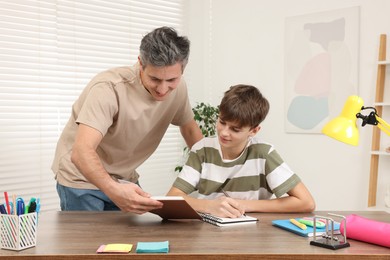 Photo of Father helping his son with homework at table indoors