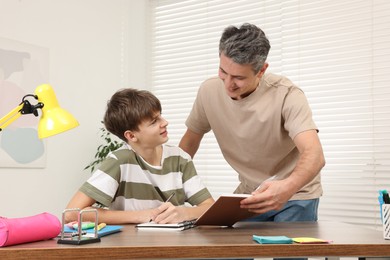 Father helping his son with homework at table indoors