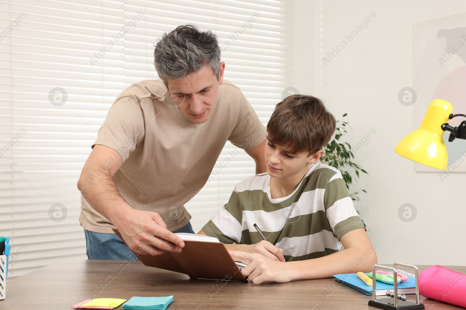 Photo of Father helping his son with homework at table indoors