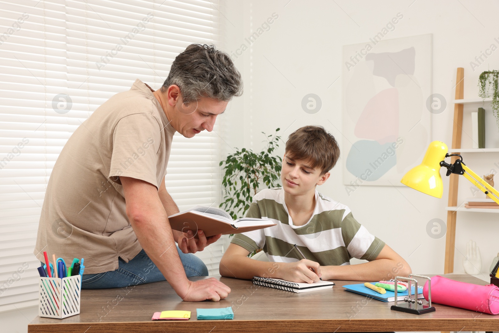 Photo of Father helping his son with homework at table indoors