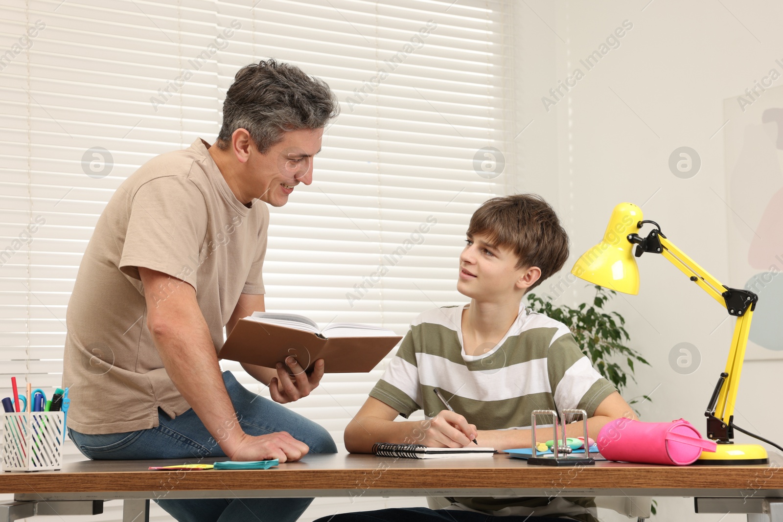 Photo of Smiling father helping his son with homework at table indoors