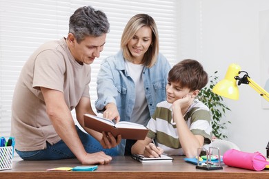 Parents helping their son with homework at table indoors