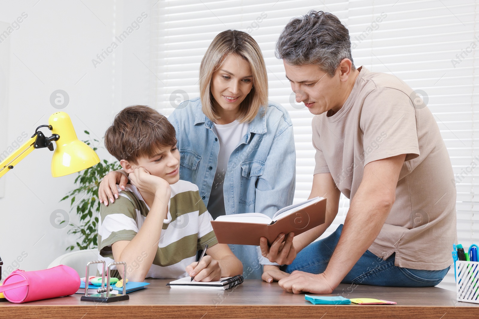 Photo of Parents helping their son with homework at table indoors